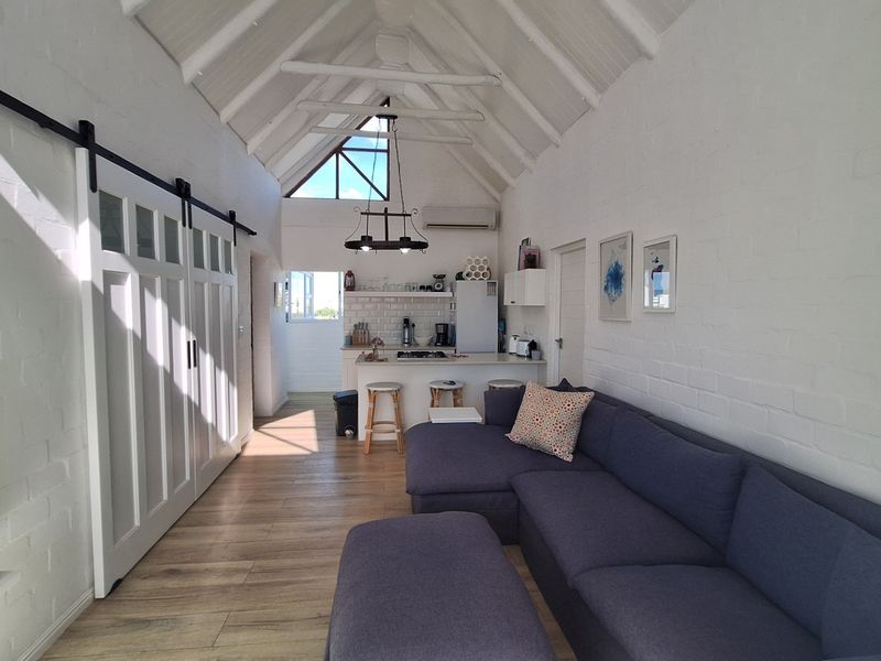 Bright open-plan living area featuring a vaulted ceiling with exposed beams, modern kitchen island, and stylish sliding barn door access.