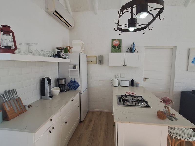 Open-plan kitchen featuring white cabinetry, stone countertops, subway tile backsplash, and a built-in gas cooktop, seamlessly integrated with the living area.