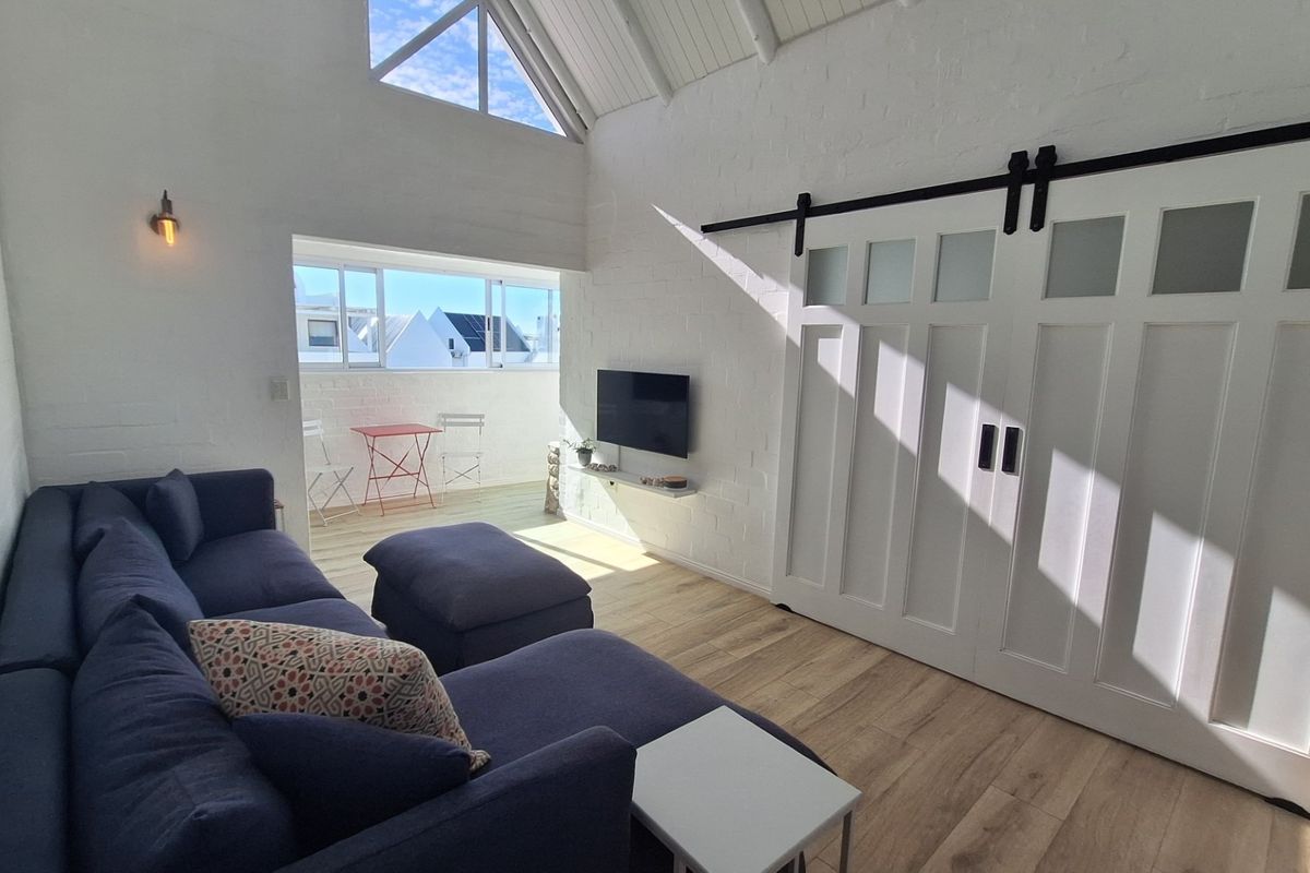 Bright living room featuring vaulted ceilings, exposed white brick walls, timber flooring, and a stylish sliding barn door leading to an adjacent space.