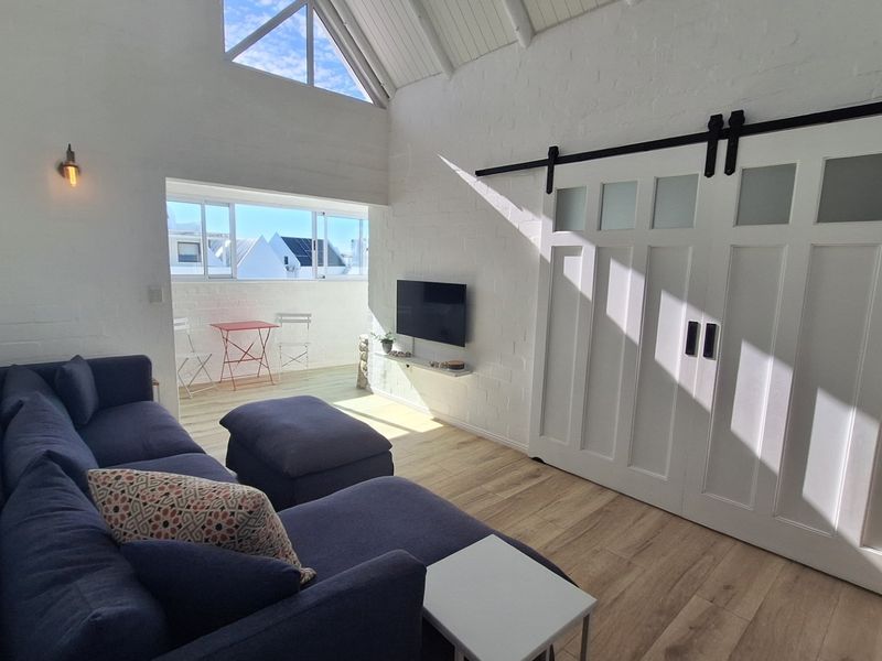 Bright living room featuring vaulted ceilings, exposed white brick walls, timber flooring, and a stylish sliding barn door leading to an adjacent space.