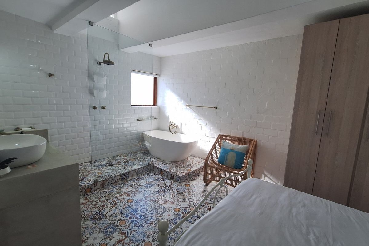 A unique bedroom suite featuring an integrated open-plan bathroom with a freestanding bathtub, glass-enclosed shower, vessel sink, and built-in wardrobe storage.