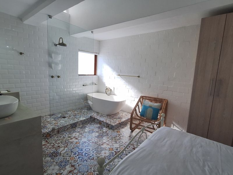 A unique bedroom suite featuring an integrated open-plan bathroom with a freestanding bathtub, glass-enclosed shower, vessel sink, and built-in wardrobe storage.
