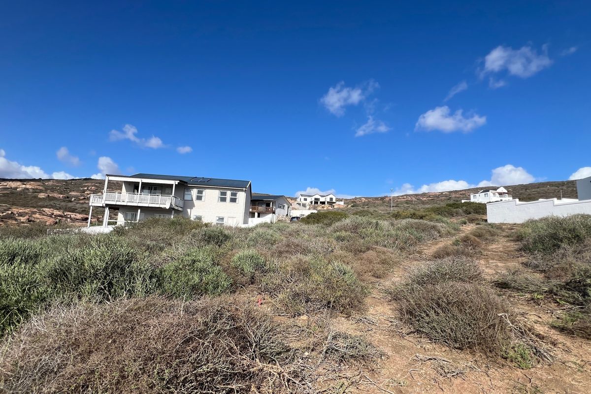 A view of a vacant residential plot featuring natural coastal vegetation with established neighboring properties visible in the background.