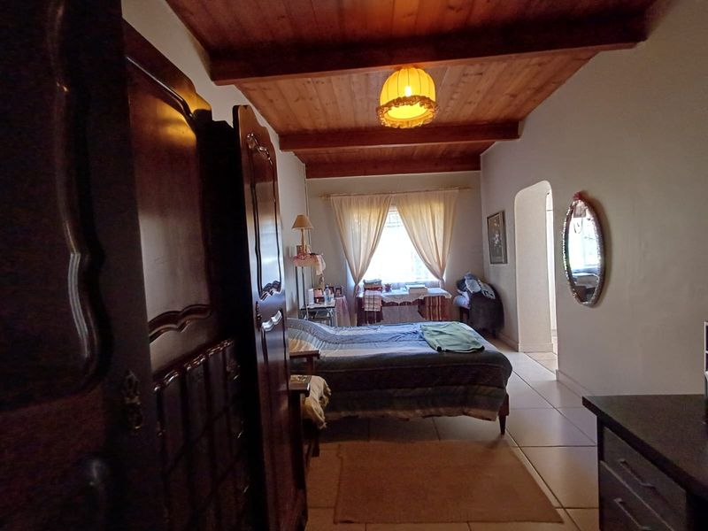 A bedroom featuring exposed timber ceiling beams, tiled flooring, and an arched doorway leading to an adjacent space.