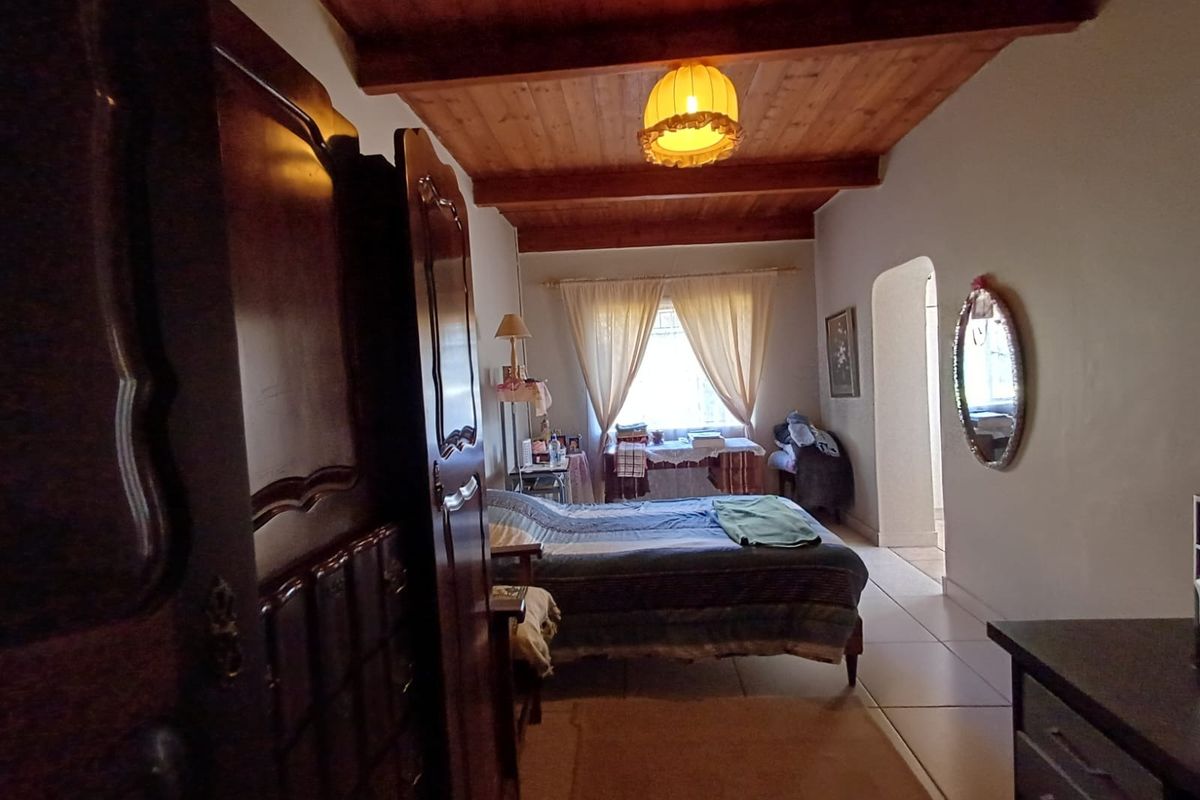 A bedroom featuring exposed timber ceiling beams, tiled flooring, and an arched doorway leading to an adjacent space.
