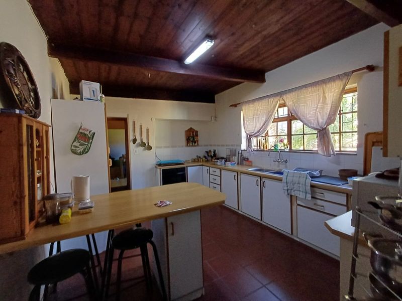 A functional kitchen featuring white cabinetry, laminate countertops, a double sink, and distinctive exposed timber ceiling beams with tiled flooring.