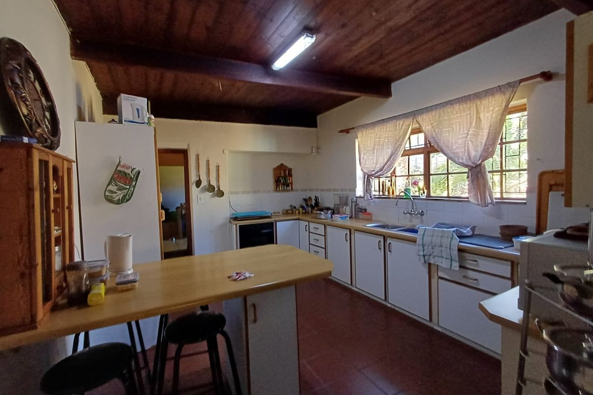 A functional kitchen featuring white cabinetry, laminate countertops, a double sink, and distinctive exposed timber ceiling beams with tiled flooring.