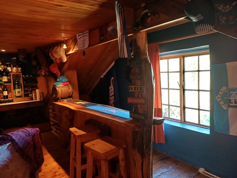 A rustic, timber-finished home bar area featuring a custom wooden counter, wood-paneled ceiling, and natural light from a timber-framed window.