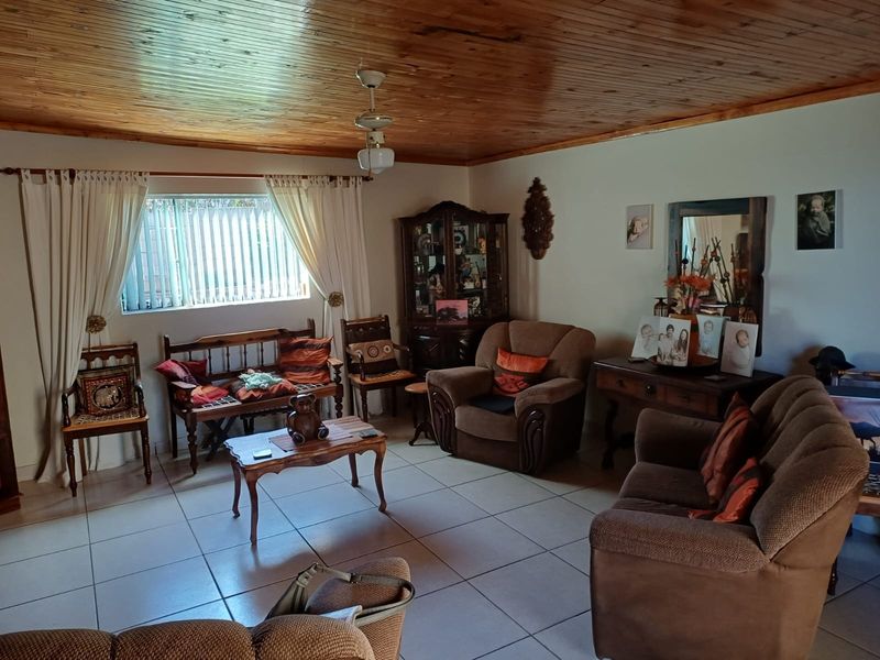 A living room featuring a timber-clad ceiling, tiled flooring, and a central ceiling fan, offering a traditional aesthetic with potential for modern updates.