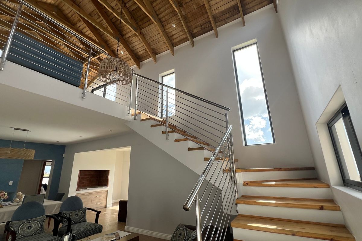 Spacious living area featuring a double-volume ceiling with exposed timber trusses, a modern timber staircase with stainless steel balustrades, and a mezzanine level.