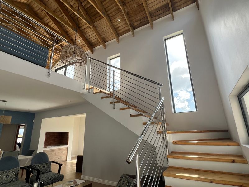 Spacious living area featuring a double-volume ceiling with exposed timber trusses, a modern timber staircase with stainless steel balustrades, and a mezzanine level.