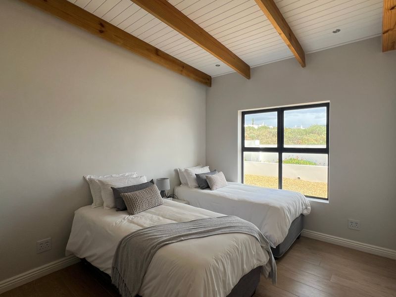 A bright bedroom featuring exposed timber ceiling beams, a white tongue and groove ceiling, laminate flooring, and a large window with an aluminium frame.
