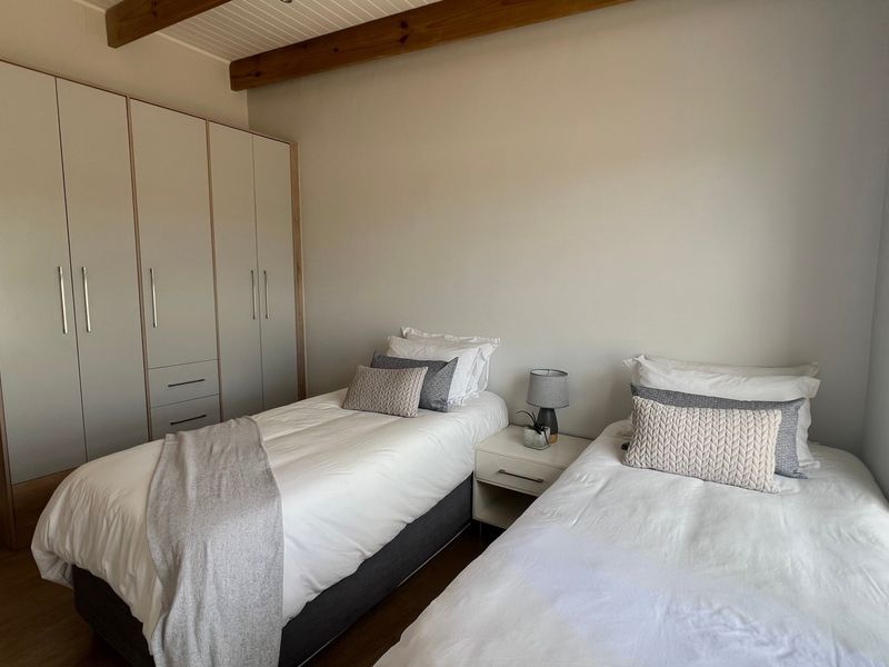 A well-maintained bedroom featuring built-in wardrobes, exposed timber ceiling beams, and modern laminate flooring.