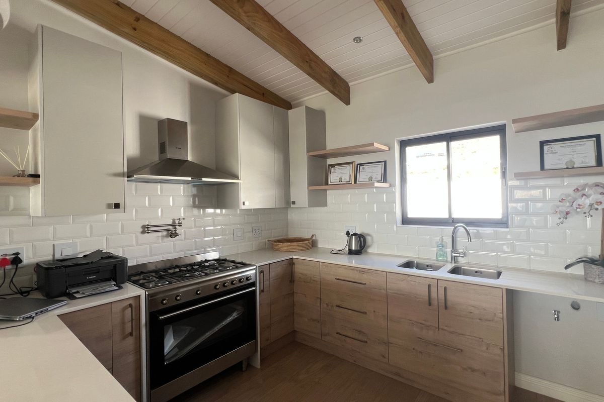 Modern kitchen featuring light wood cabinetry, stone countertops, subway tile backsplash, gas stove with extractor, and exposed timber ceiling beams.