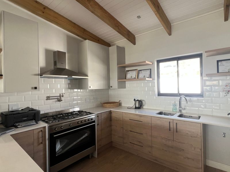 Modern kitchen featuring light wood cabinetry, stone countertops, subway tile backsplash, gas stove with extractor, and exposed timber ceiling beams.