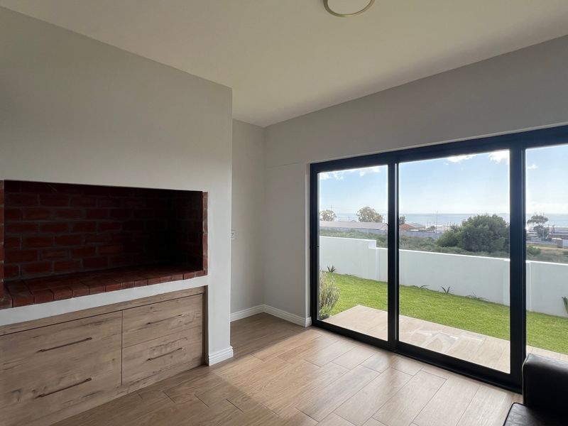 Bright living area featuring a built-in brick fireplace, modern cabinetry, and large sliding doors opening to a garden with coastal views.