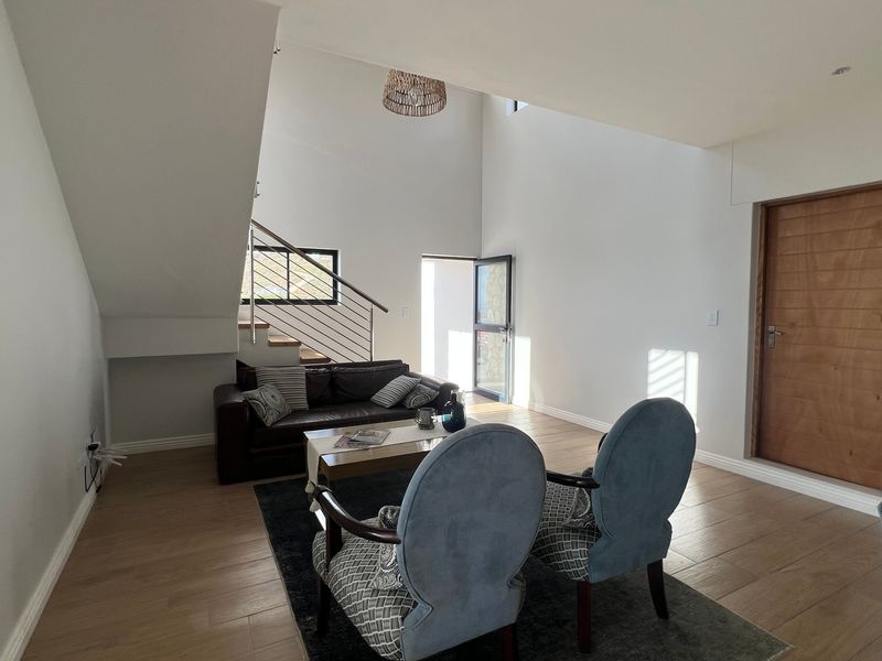 Spacious living area featuring high ceilings, modern laminate flooring, a staircase with a stainless steel balustrade, and a solid wood door.