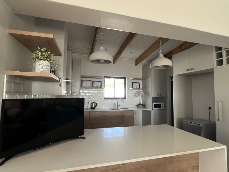 Modern kitchen featuring timber ceiling beams, subway tile backsplash, stone countertops, and ample built-in cabinetry with floating shelving.