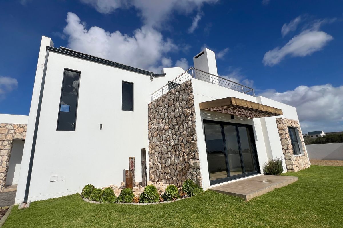 Modern rear exterior view featuring stone cladding, a timber pergola, a balcony with stainless steel railings, and well-maintained garden space.