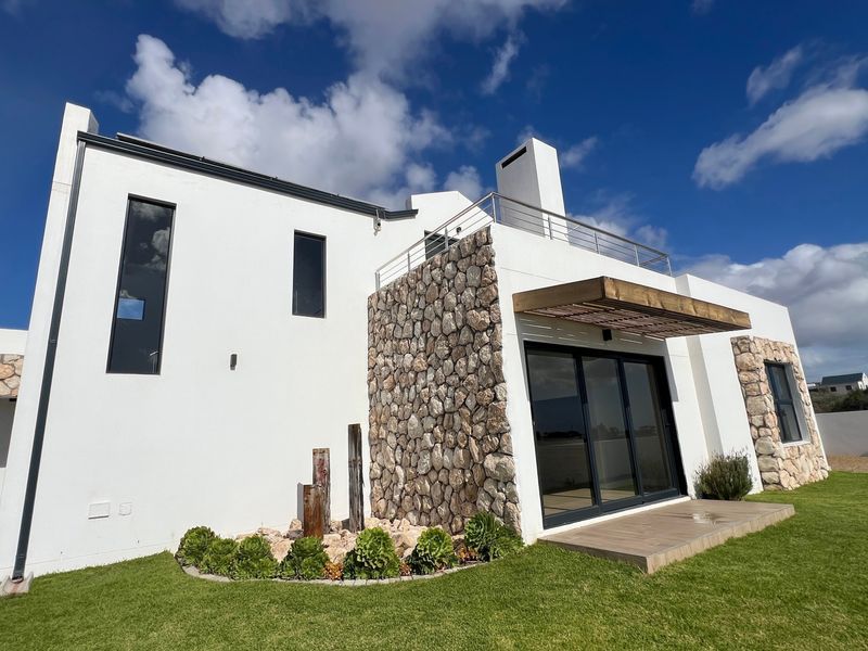 Modern rear exterior view featuring stone cladding, a timber pergola, a balcony with stainless steel railings, and well-maintained garden space.