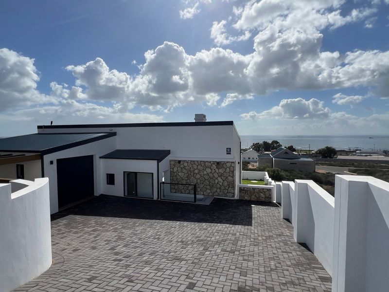 Modern coastal home featuring a paved driveway, stone-clad facade, and garage, set against a scenic ocean view.