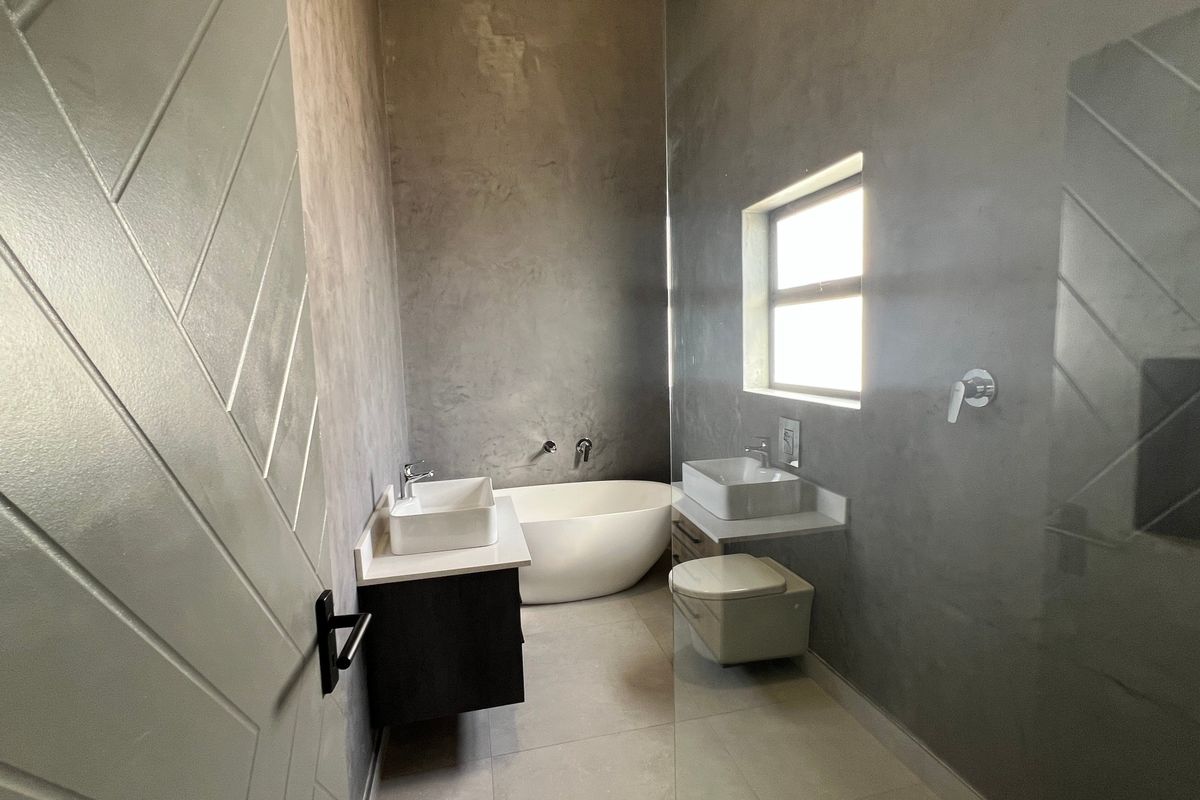 Modern bathroom featuring a freestanding bathtub, dual vessel sinks on wall-mounted vanities, wall-mounted toilet, and contemporary grey cementitious wall finishes.