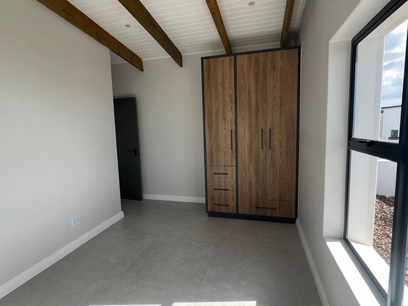 A bright, modern bedroom featuring tiled floors, exposed timber ceiling beams, and a sleek built-in wooden wardrobe.
