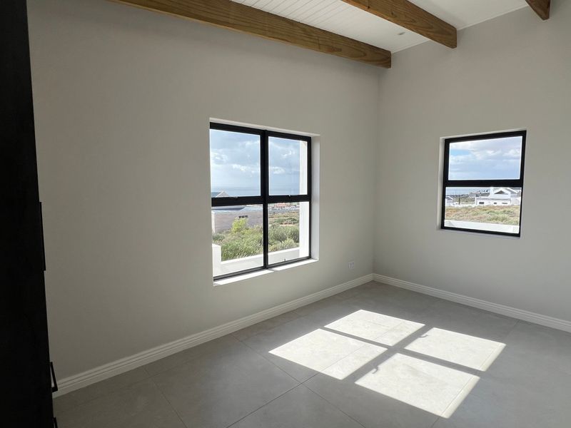 A bright, empty bedroom featuring modern tiled flooring, exposed timber ceiling beams, and black-framed windows with natural light.