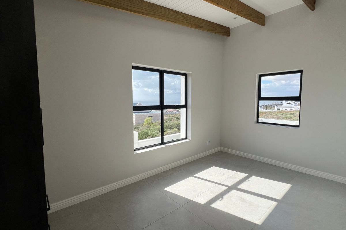 A bright, empty bedroom featuring modern tiled flooring, exposed timber ceiling beams, and black-framed windows with natural light.