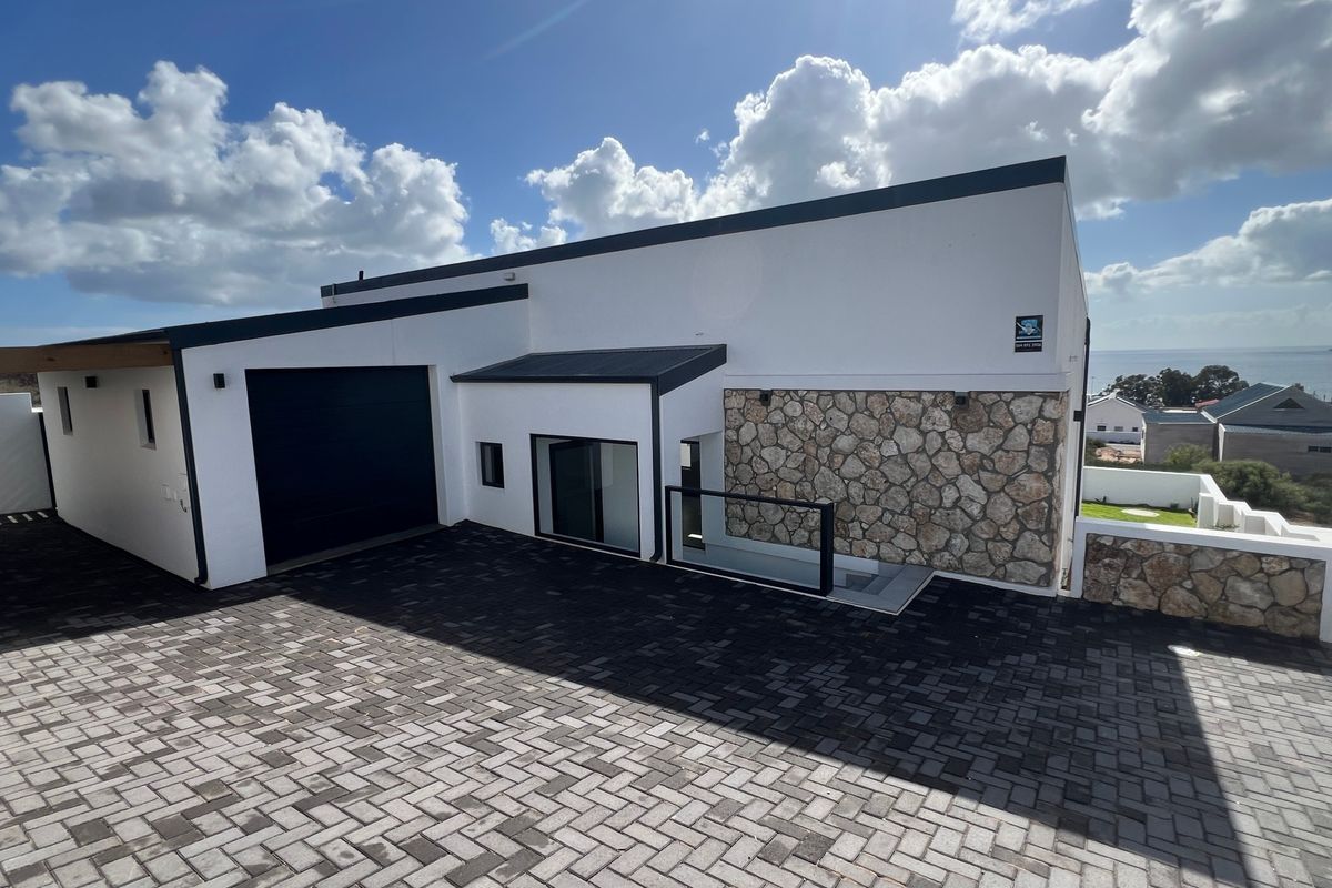 Modern architectural front facade featuring stone cladding, a paved driveway, and a sleek garage door with coastal views in the background.