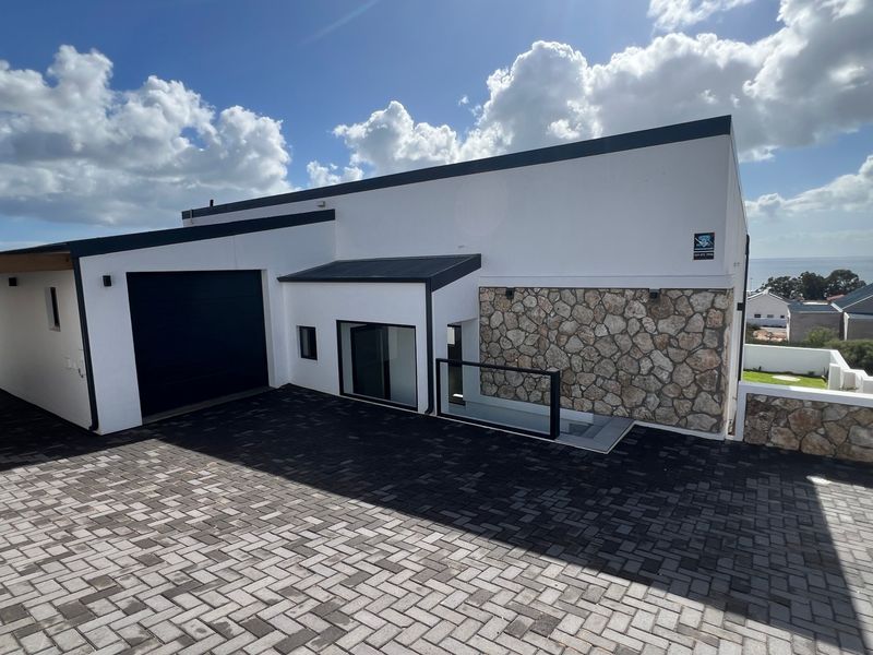 Modern architectural front facade featuring stone cladding, a paved driveway, and a sleek garage door with coastal views in the background.