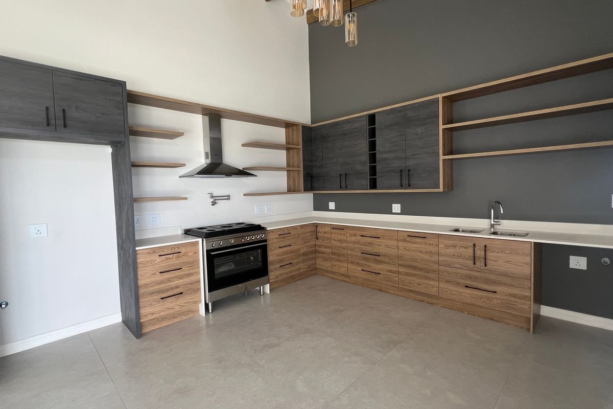 Modern kitchen featuring two-tone cabinetry, stone countertops, stainless steel stove with extractor, double sink, and open shelving in a spacious, light-filled layout.