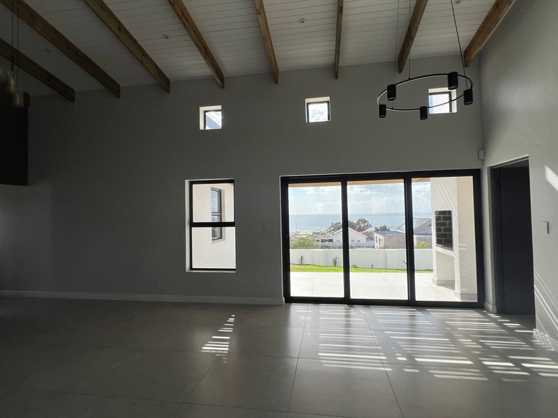 Spacious open-plan living area featuring high ceilings with exposed timber beams, large sliding doors leading to a patio, and modern tiled flooring.