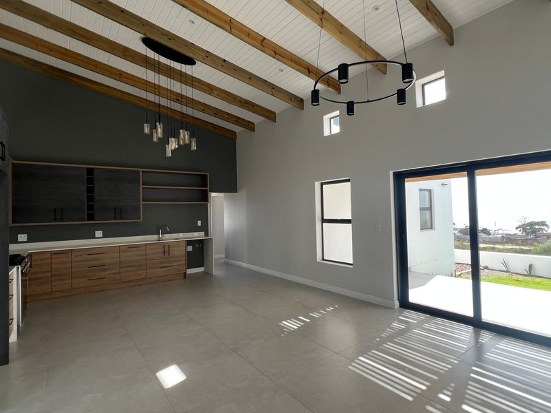 Spacious open-plan living area featuring vaulted ceilings with exposed timber beams, modern cabinetry, tiled floors, and large sliding doors leading to an outdoor space.