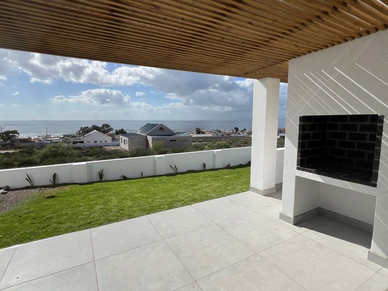Covered patio featuring a built-in braai, timber slat ceiling, and tiled flooring, overlooking a private lawn with expansive coastal views.