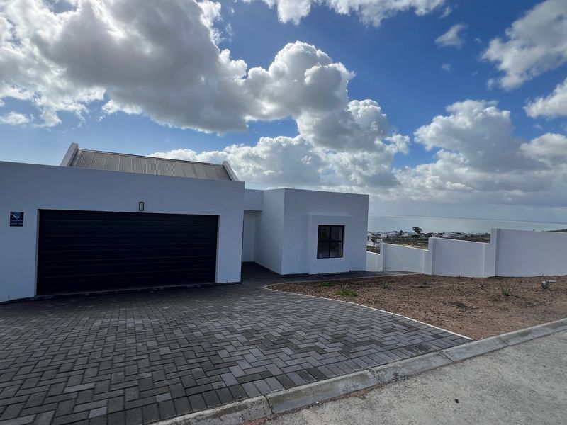Modern front elevation featuring a paved driveway, double garage, and clean white exterior finishes with a view of the surrounding landscape.