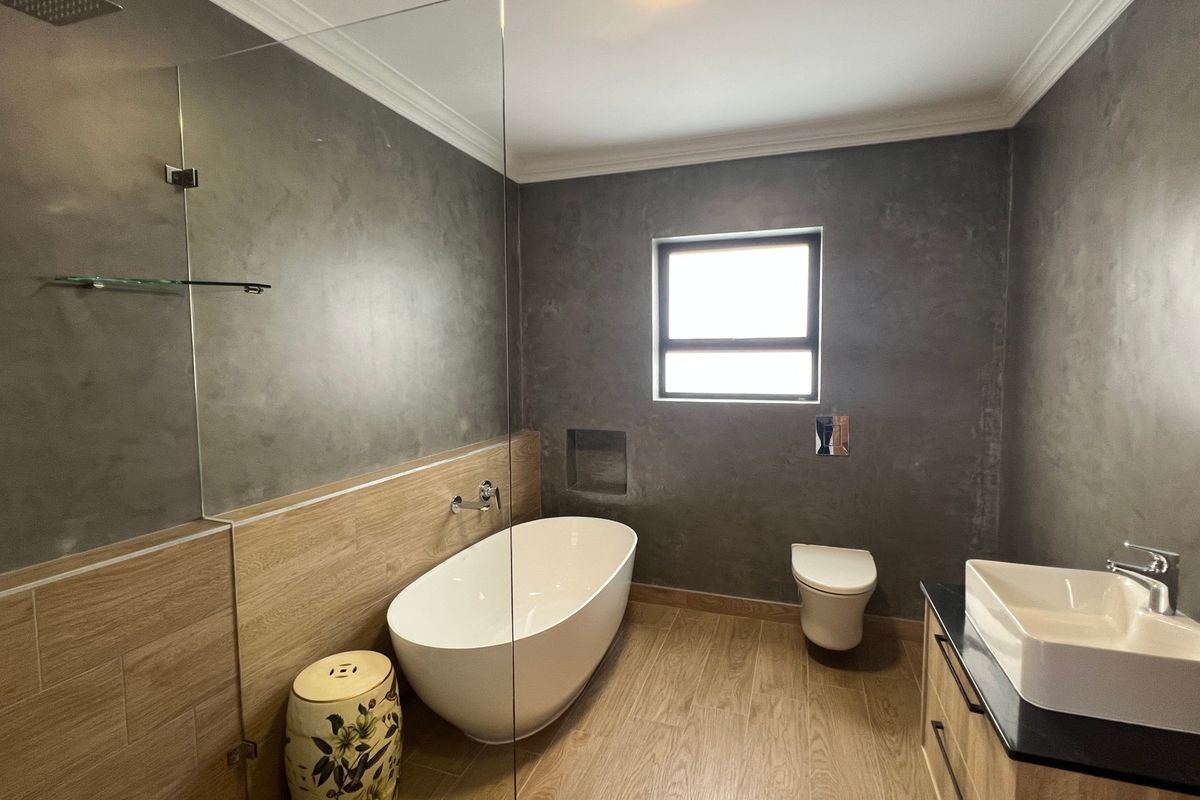 Modern bathroom featuring a freestanding bathtub, wall-hung toilet, vessel sink vanity, and contemporary cement-look wall finishes with wood-look tile flooring.