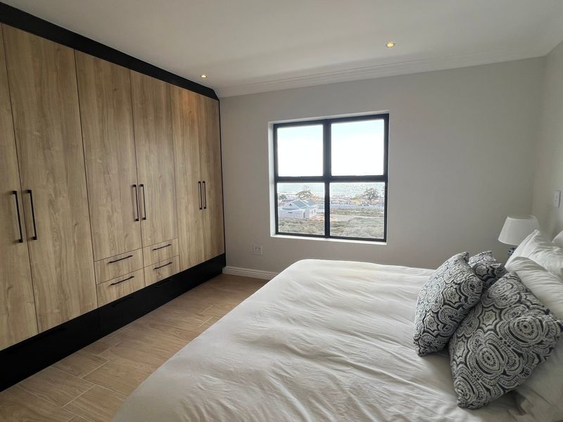 A well-maintained bedroom featuring modern wood-finish built-in cupboards, tiled flooring, and a window offering scenic views.