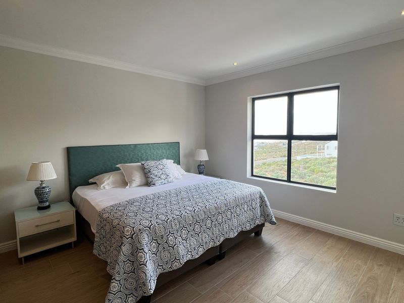 A well-maintained bedroom featuring wood-look tile flooring, built-in wardrobes, recessed downlights, and a large window with natural light.