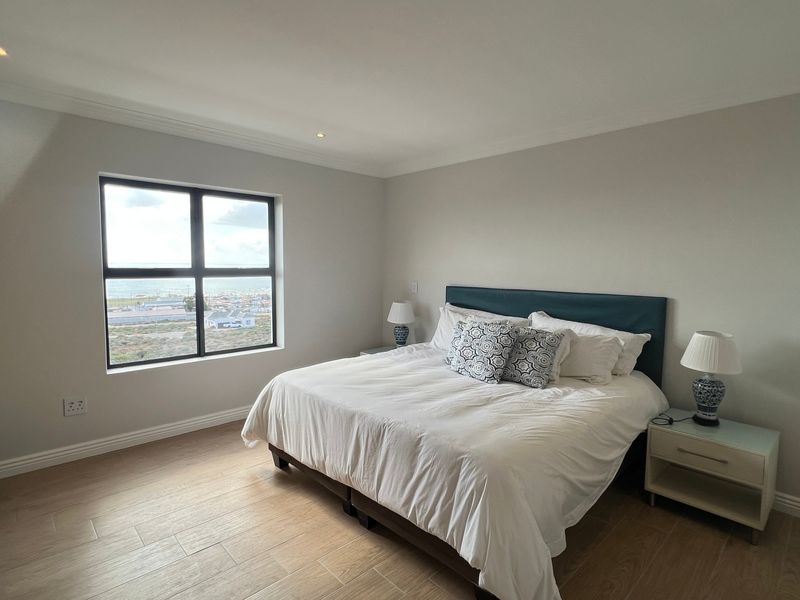 A well-maintained bedroom featuring light-toned tiled flooring, built-in cupboards, recessed lighting, and a window offering an elevated coastal view.