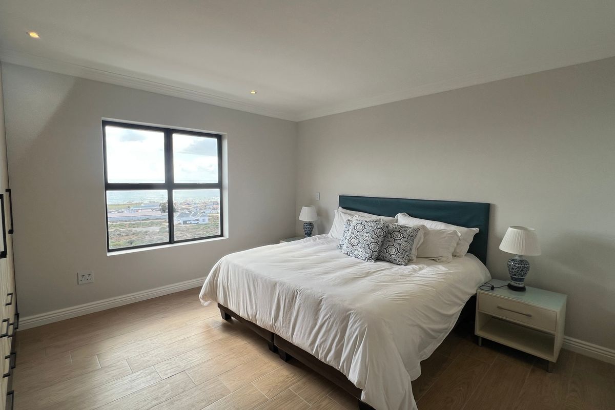 A well-maintained bedroom featuring light-toned tiled flooring, built-in cupboards, recessed lighting, and a window offering an elevated coastal view.