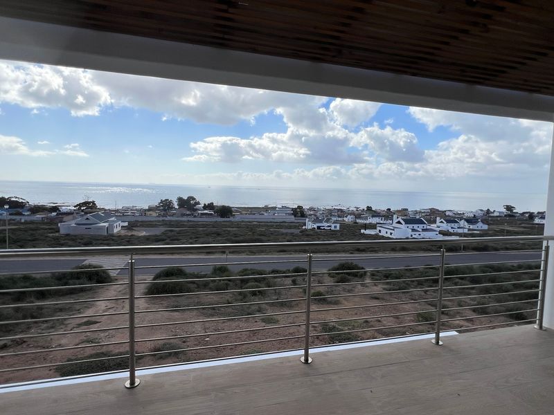 A spacious covered balcony featuring a modern stainless steel balustrade, timber slat ceiling, and panoramic coastal views.