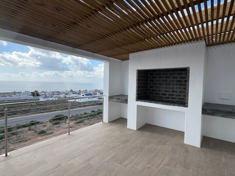 Covered balcony featuring a built-in braai, concrete prep surfaces, timber slat ceiling, and stainless steel balustrade with expansive coastal views.