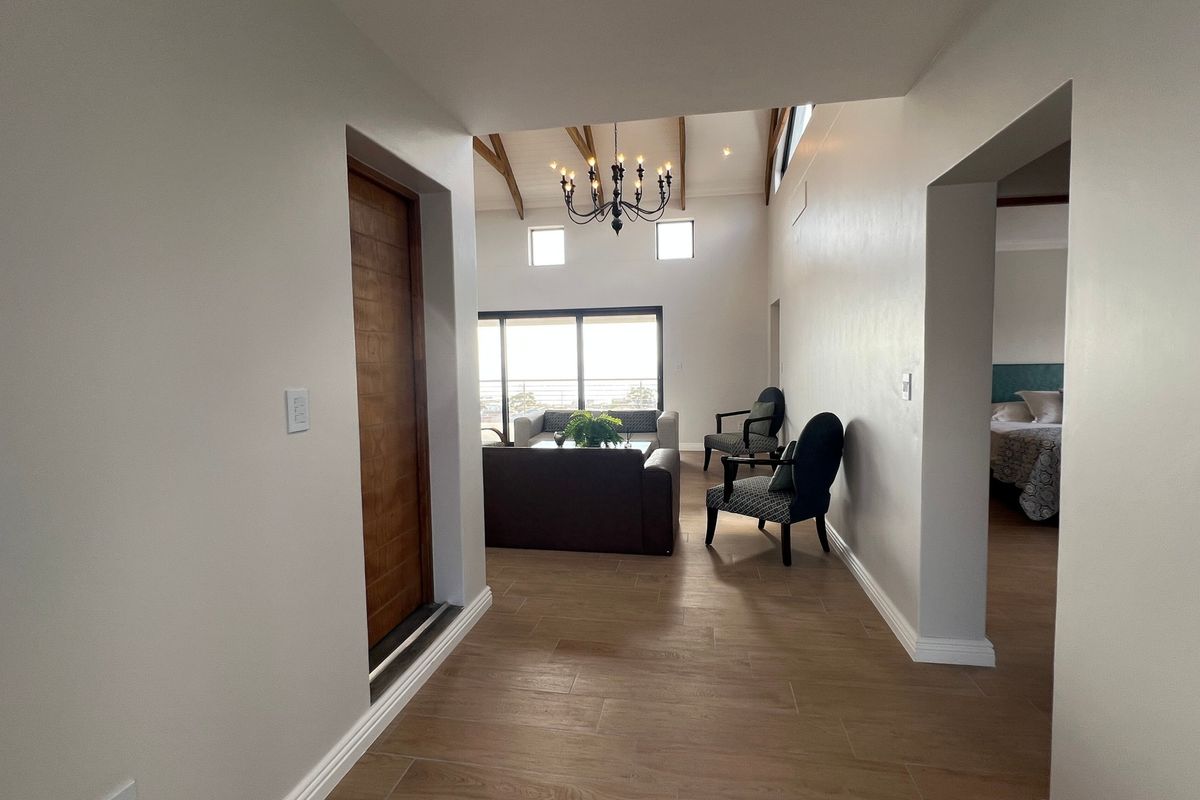A bright hallway featuring tiled flooring and exposed timber ceiling beams, leading into an open-plan living area with access to a balcony.