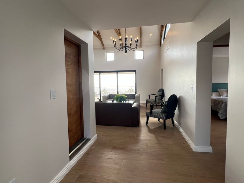 A bright hallway featuring tiled flooring and exposed timber ceiling beams, leading into an open-plan living area with access to a balcony.