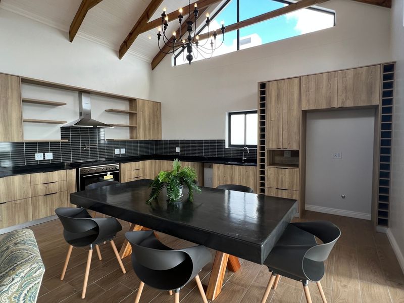 Spacious open-plan kitchen featuring vaulted ceilings with exposed timber beams, modern wood-finish cabinetry, integrated appliances, and a sleek tiled backsplash.
