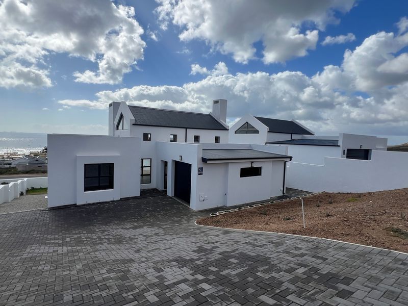 Modern white architectural home featuring a paved driveway, integrated garage, and clean lines, set against a coastal backdrop.