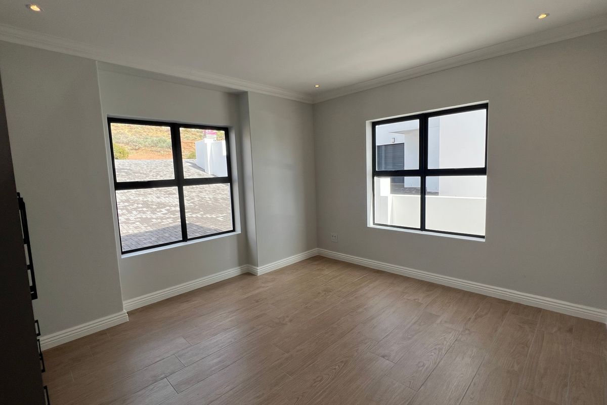 A bright, empty bedroom featuring modern wood-look tile flooring, neutral walls, recessed lighting, and black aluminium-framed windows.