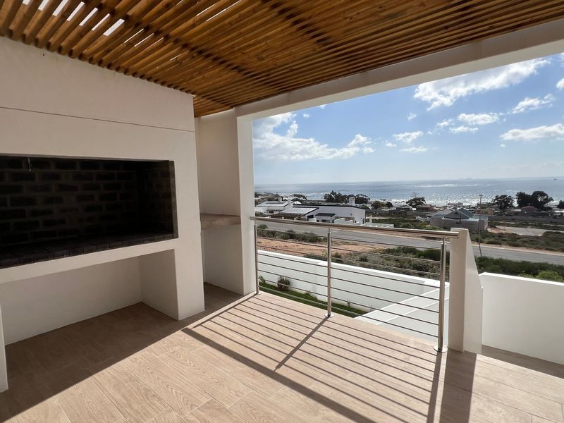 Covered balcony featuring a built-in braai, timber slat pergola, and stainless steel balustrade, offering expansive coastal views.