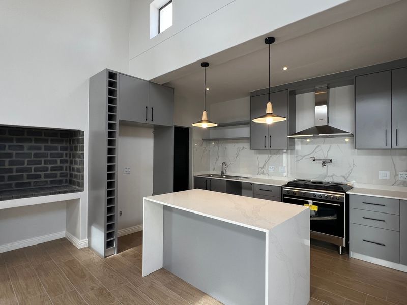 Modern open-plan kitchen featuring sleek grey cabinetry, stone countertops, a central island, built-in fireplace, and high-end stainless steel appliances.